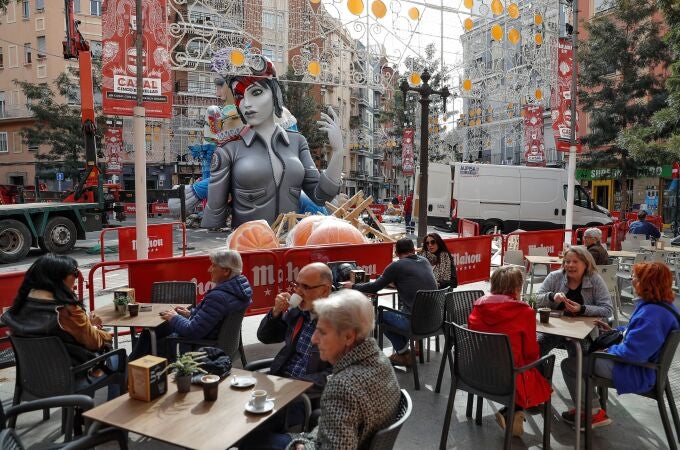 Varias personas disfrutan de un café en una terraza ante una de las numerosas fallas del barrio de Ruzafa, a la espera de los días grandes a partir de este próximo fin de semana