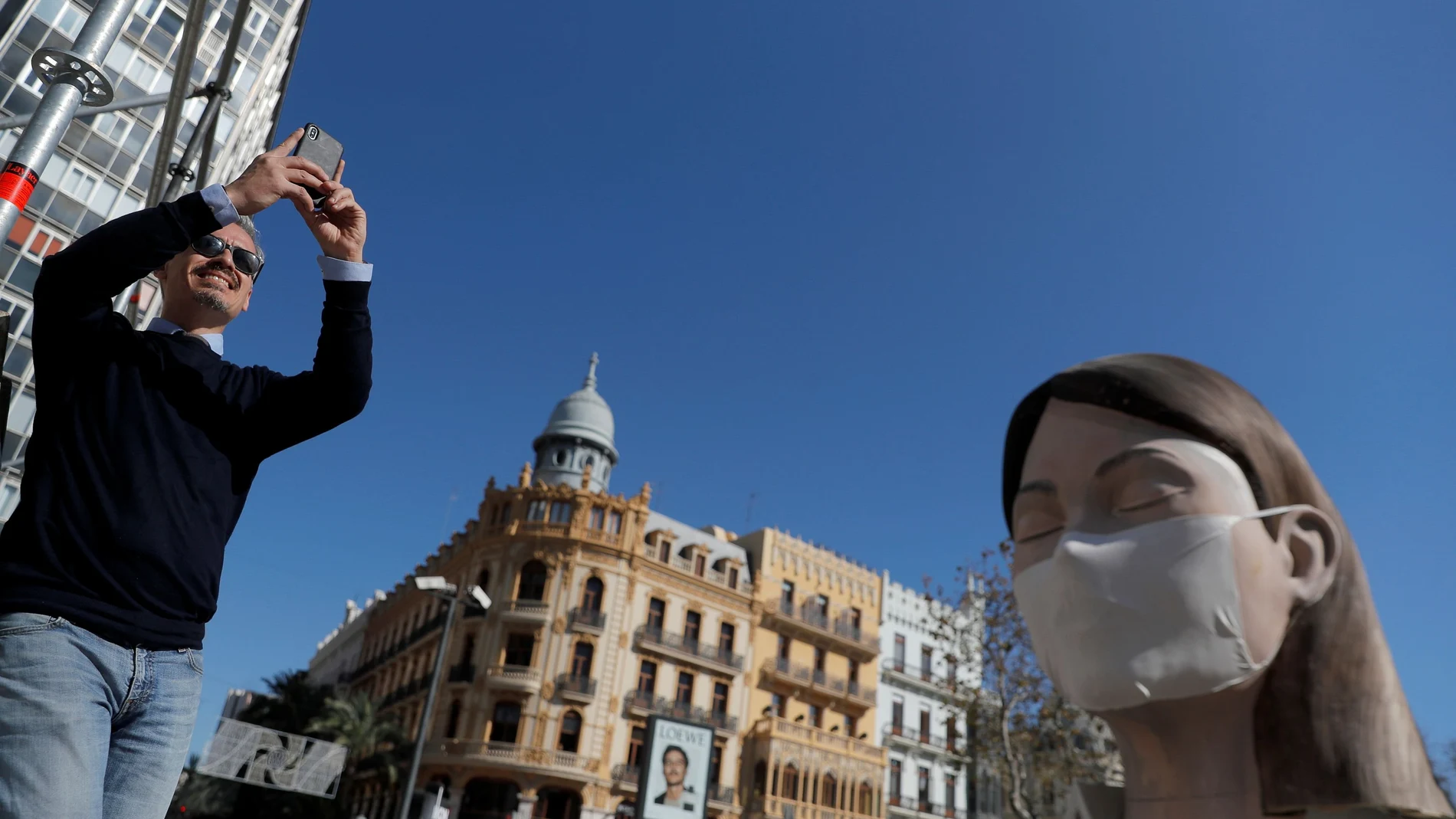 A man takes pictures next to a monument displayed with a protective mask, after regional authorities postponed the Fallas Festival amidst coronavirus concerns in Valencia