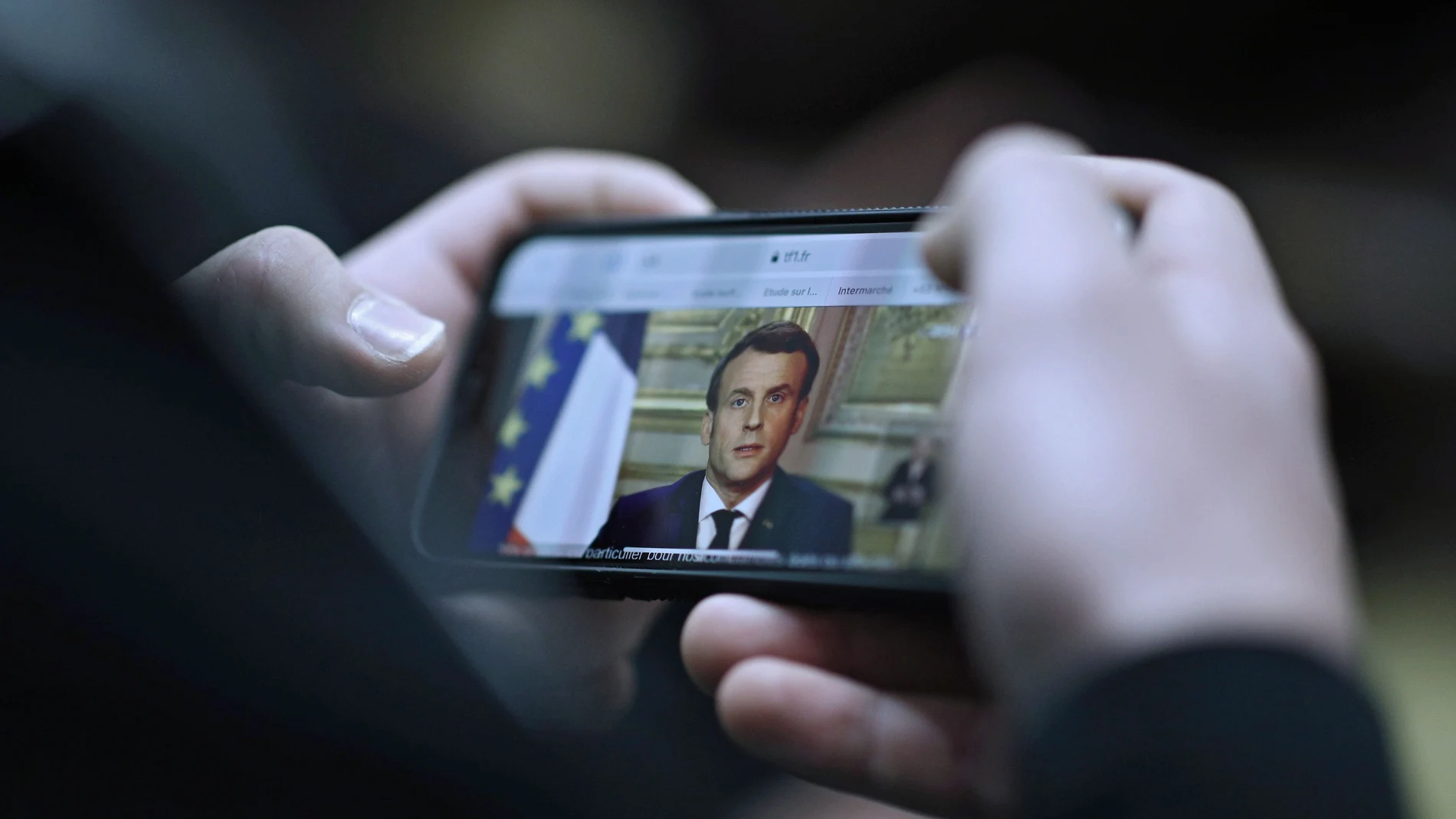 Una francés ve por el móvil el discurso a la nación del presidente Emmanuel Macron/REUTERS