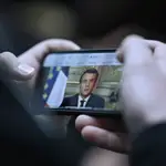 Una francés ve por el móvil el discurso a la nación del presidente Emmanuel Macron/REUTERS