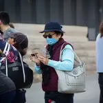 Una mujer usa su móvil protegida con mascarilla ante el avance del coronavirus en Barcelona
