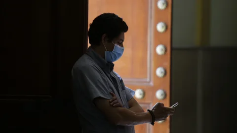 Un hombre observa su teéfono con una mascarilla para protegerse frente al coronavirus