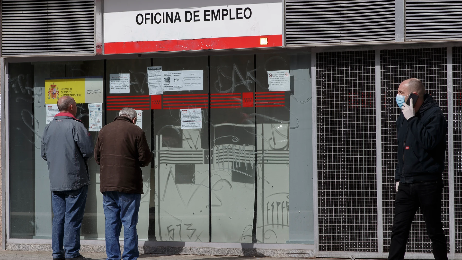 Dos ancianos leen los carteles de una oficina de empleo cerrada durante el estado de alarma en España