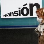 Una mujer con una mascarilla camina junto una sucursal bancaria de Madrid
