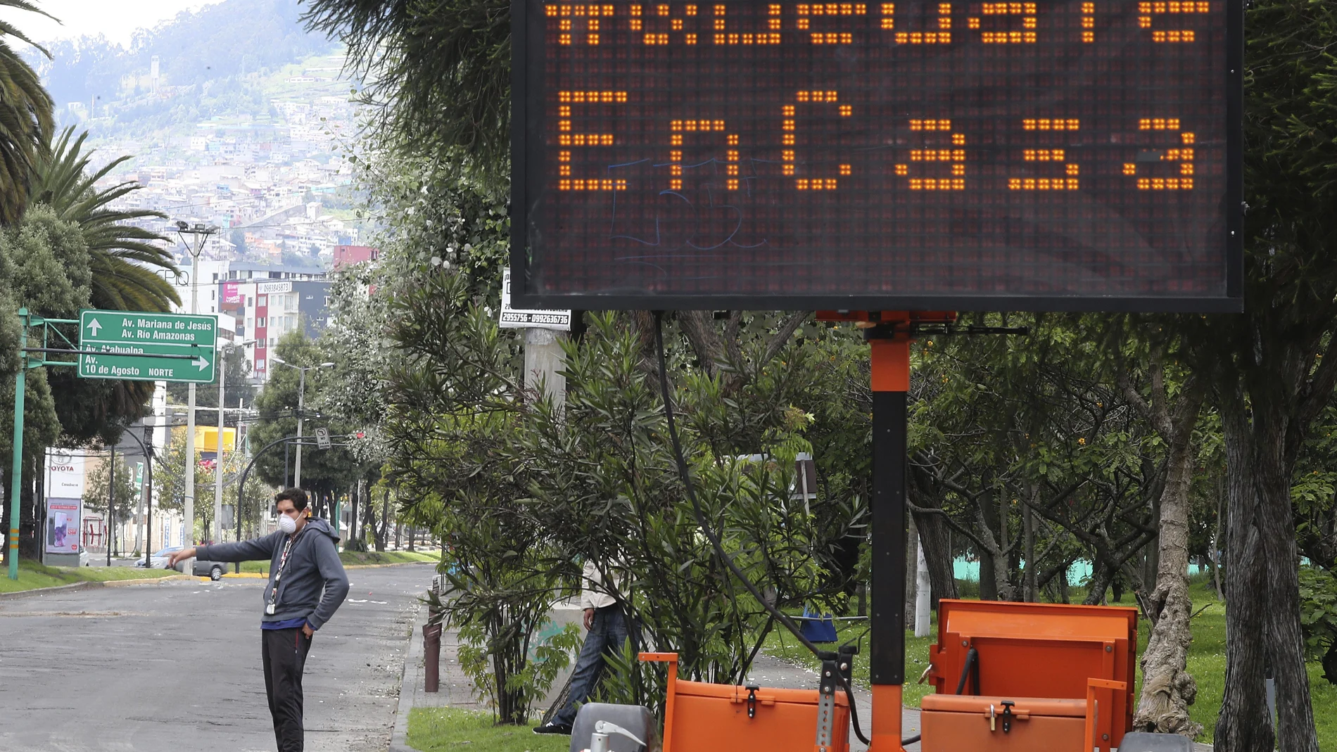 An electronic road sign reads in Spanish "Stay at home" where a man hails a cab in Quito, Ecuador, Thursday, March 19, 2020. The government is restricting movement to those who provide basic services, is enforcing a curfew, and closing schools, to help contain the spread of the new coronavirus. (AP Photo/Dolores Ochoa)
