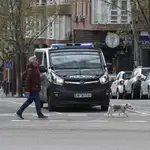 Un hombre pasa con su perro ante un vehículo de la Policía Nacional en la Calle Ribera de Curtidores