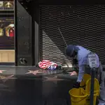 Un empleado de la limpieza trabaja en el bulevard de Hollywood mientras un &quot;homeless&quot; duerme cubierto por la bandera e EE UU