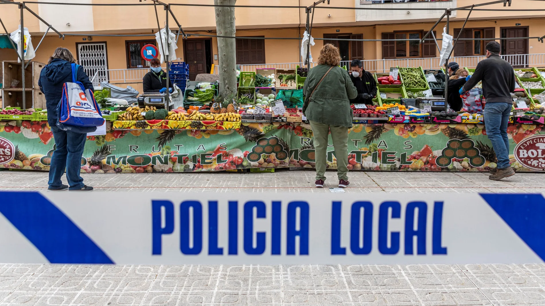 Miembros de la Policia Local y Voluntarios de Protección Civil se encargan de que se cumplan las medidas de seguridad durante el mercado semanal de Andraxt, en Mallorca, este miércoles, repartiendo guantes a los compradores y ocupándose de que respete un metro de distancia entre compradores y vendedores.