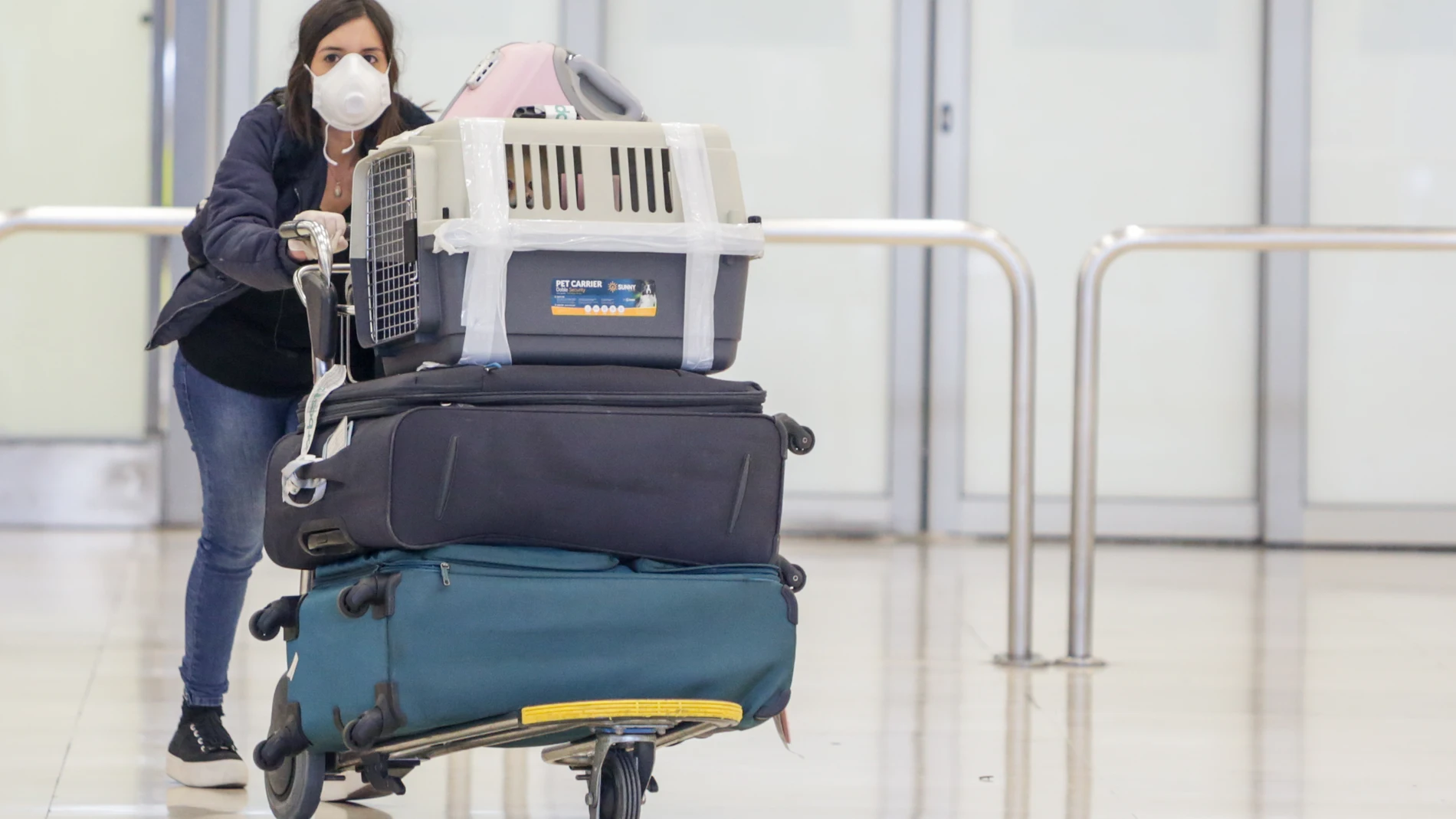 Una mujer protegida con mascarilla recoge su equipaje