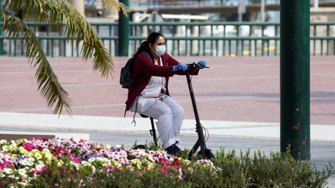 Una trabajadora de desplaza en un patinete protegida con una mascarilla por una calle de Málaga. EFE/Daniel Pérez