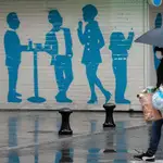 Una persona, protegida con mascarilla, vuelve del supermercado, bajo la lluvia