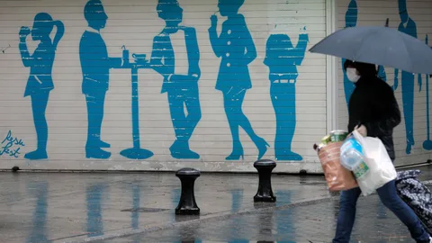 Una persona, protegida con mascarilla, vuelve del supermercado, bajo la lluvia