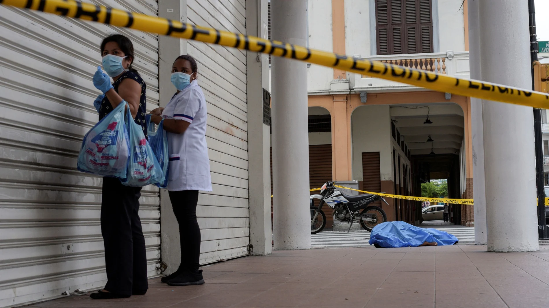 El cadaver de un hombre que colapso en una calle de Guayaquil, Ecuador custodiado por dos mujeres a la espera de los servicios funerarios.