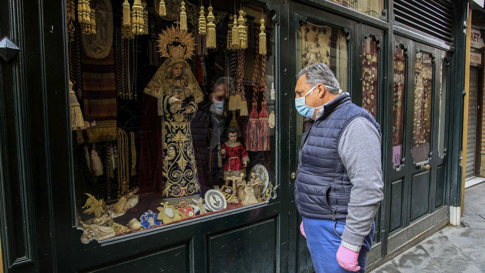 Un hombre con mascarilla contempla el escaparate de una tienda cofrade