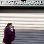 Una persona con mascarilla pasa por uno de los bares y restaurantes que permanecen cerrados en Valencia