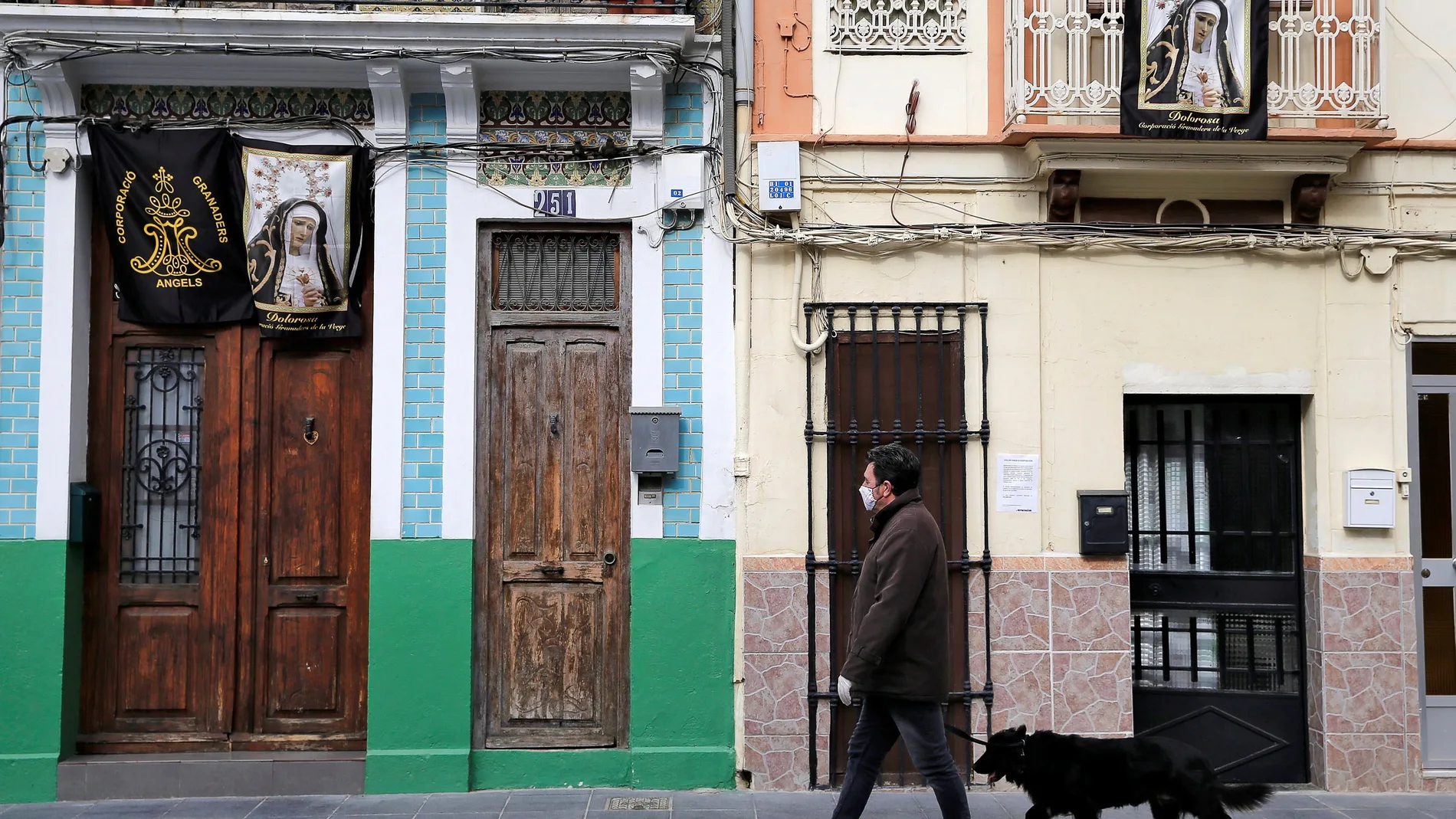 Un hombre pasa ante dos casas con imágenes de la Virgen mientras pasea a su perro en Valencia