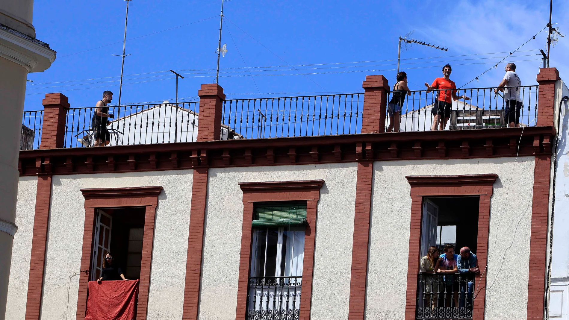 Un grupo de personas se asoman a los balcones y la azotea de sus viviendas durante el confinamiento en Sevilla