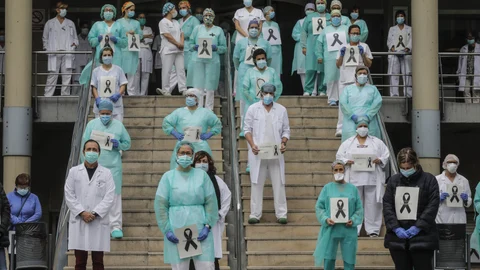 Sanitarios protegidos con mascarillas sujetan crespones negros durante el minuto de silencio en la entrada del Hospital Doctor Peset por la técnica de enfermería fallecida por coronavirus