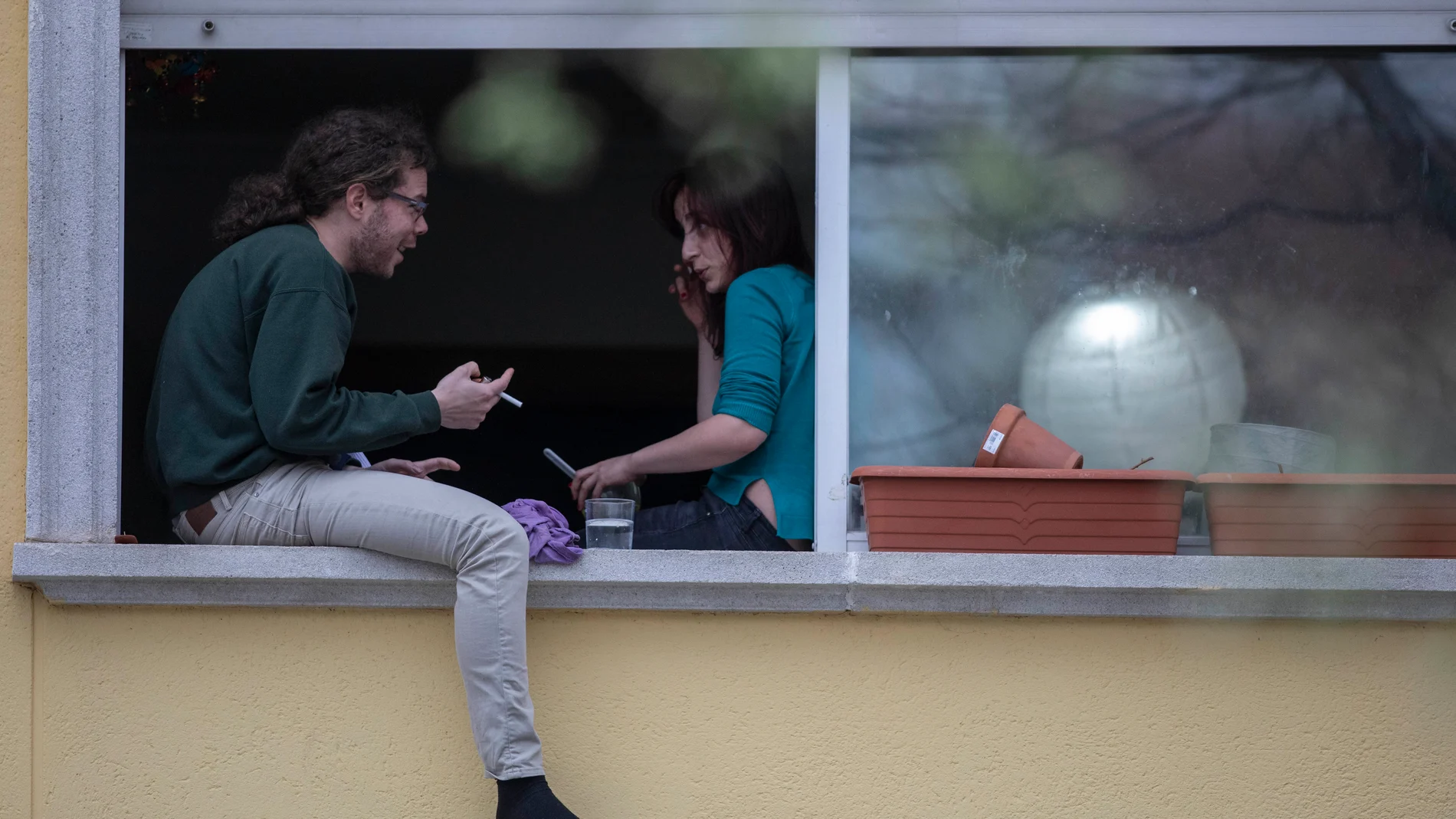 Dos vecinos del madrileño barrio Puente de Vallecas conversan sentados en la ventana de su casa
