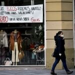 Una mujer con mascarilla pasa delante de la tienda de un escaparate en Pamplona con un mensaje de ánimo