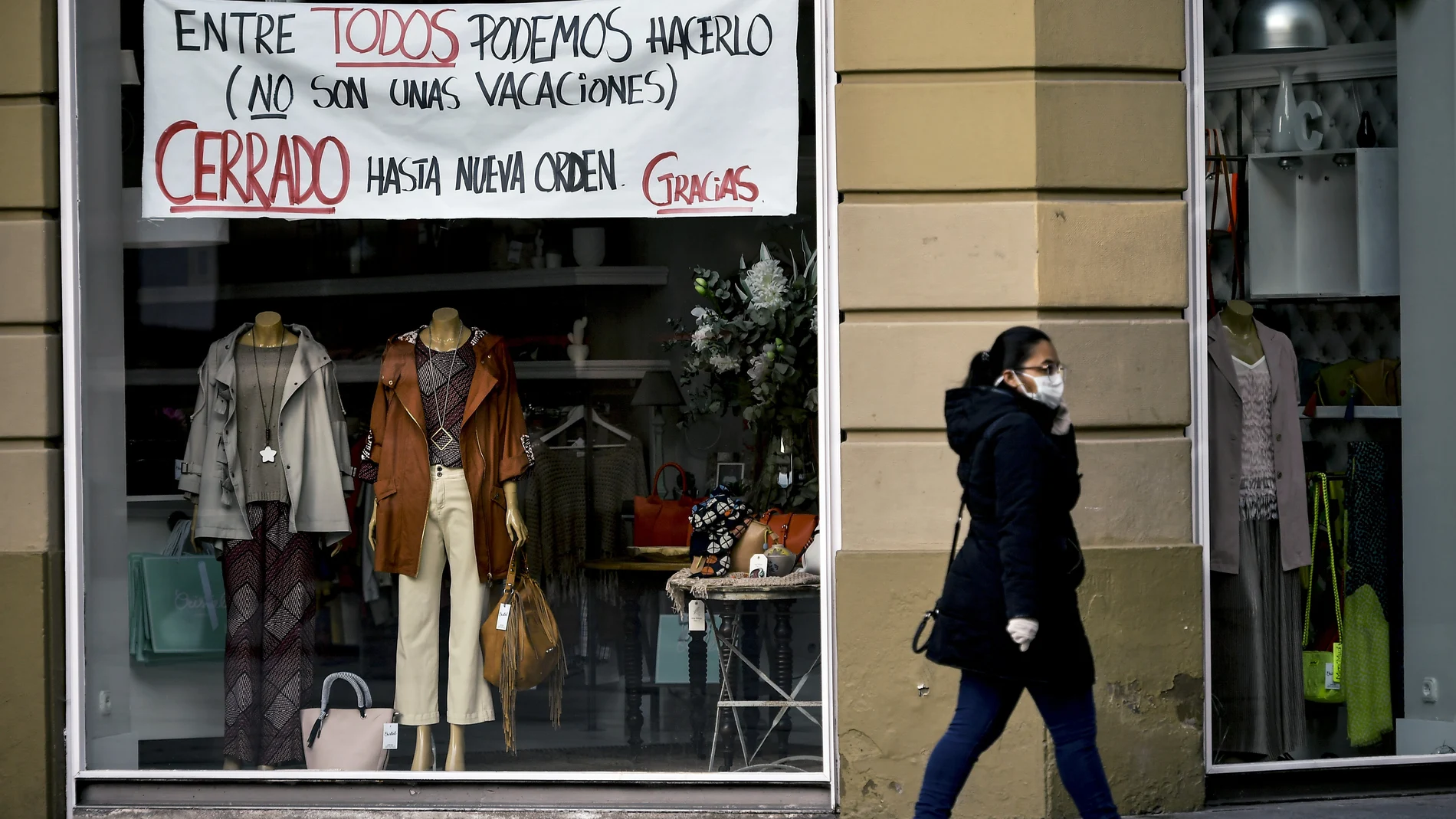 Una mujer con mascarilla pasa delante de la tienda de un escaparate en Pamplona con un mensaje de ánimo