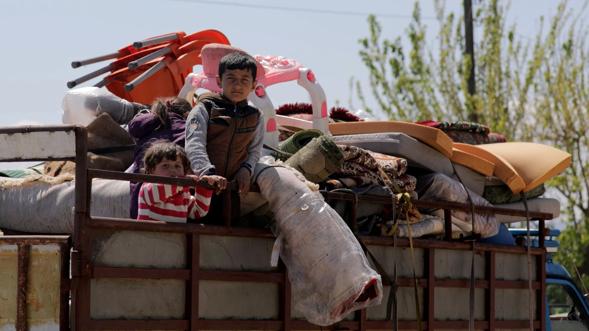 Displaced Syrian children ride on a back of a truck as they move back home, as some people are afraid of the coronavirus disease (COVID-19) outbreak in crowded camps, in Dayr Ballut
