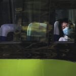 Una mujer con mascarilla mira por la ventana desde el autobús en Pekín