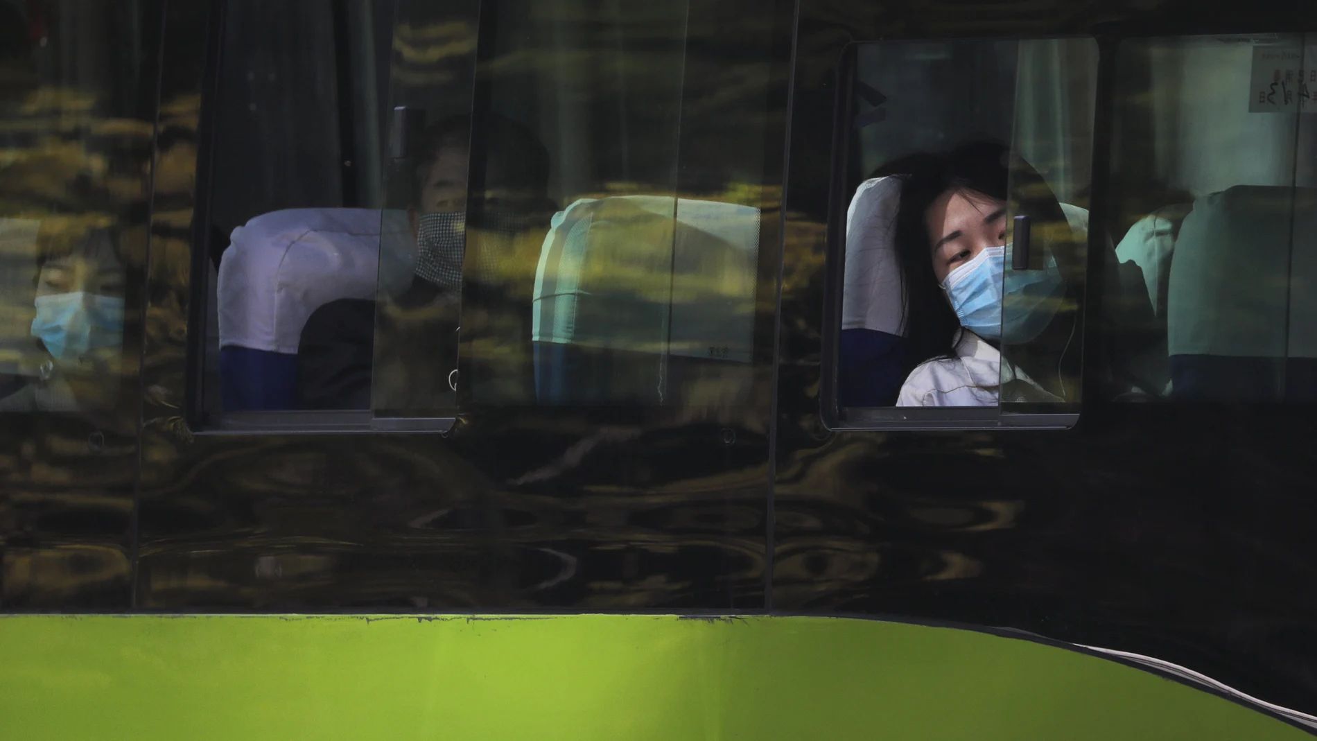 Una mujer con mascarilla mira por la ventana desde el autobús en Pekín
