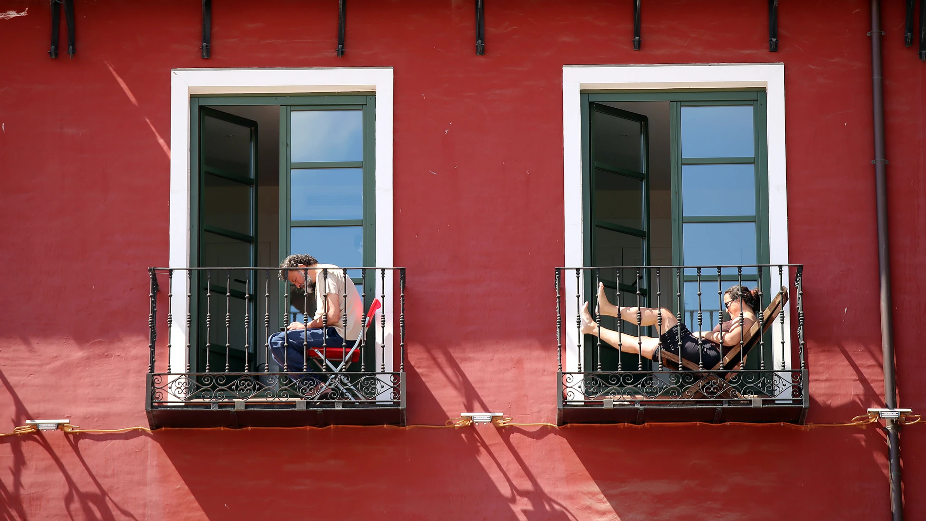 Dos personas toman el sol en el balcón de su vivienda en la Plaza Mayor de Valladolid
