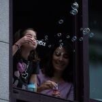 Una niña hace pompas de jabón en una ventana de su vivienda, hoy martes en Ourense. Los niños de hasta 14 años podrán salir a partir del 26 de abril a dar paseos, con lo que el Gobierno rectifica la medida aprobada esta misma mañana.