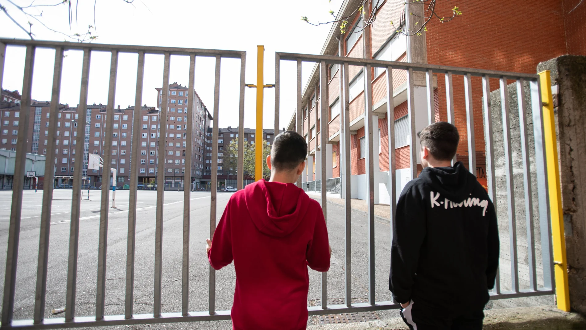 Dos adolescentes observan el patio cerrado de un colegio