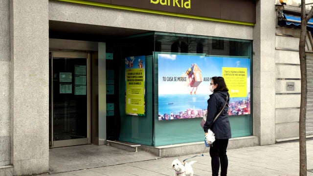 Una mujer pasea con un perro frente a una sucursal de Bankia