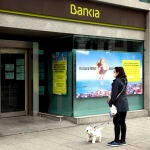 Una mujer pasea con un perro frente a una sucursal de Bankia