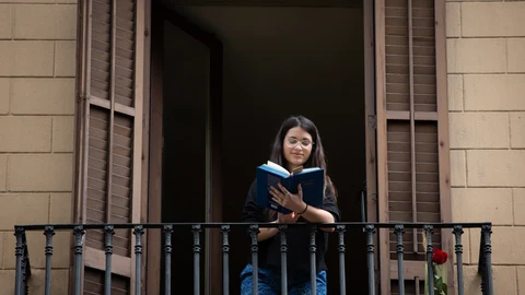 Una joven lee un libro en el balcón de su casa