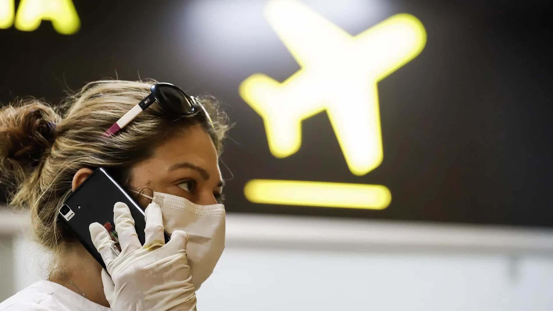 Una mujer con mascarilla y guantes habla por teléfono antes de coger un avión