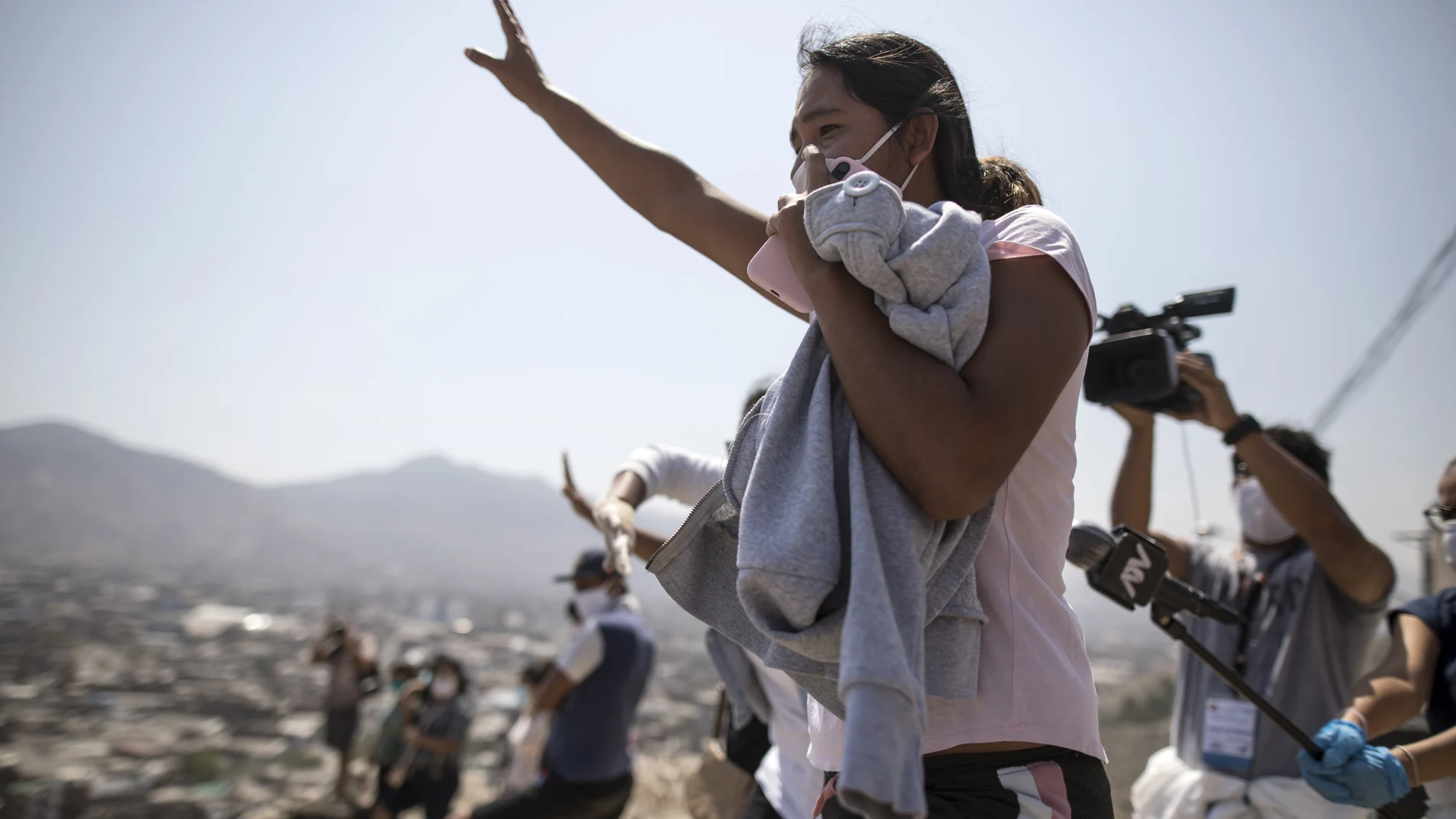 From the top of a hill, a woman shouts at a relative who is an inmate at the Lurigancho prison during a prison protest, in Lima, Peru, Tuesday, April 28, 2020. Inmates complain that authorities are not doing enough to prevent the spread of the new coronavirus inside the prison. (AP Photo/Rodrigo Abd)