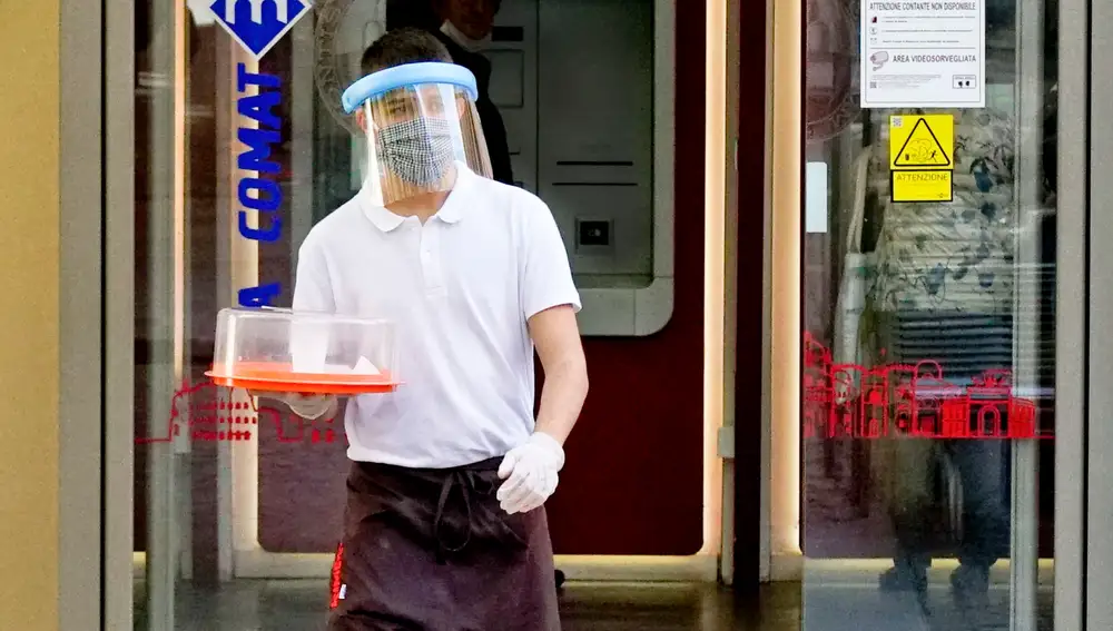 Un camarero con mascarilla y protector lleva el café en Nápoles, al sur de Italia