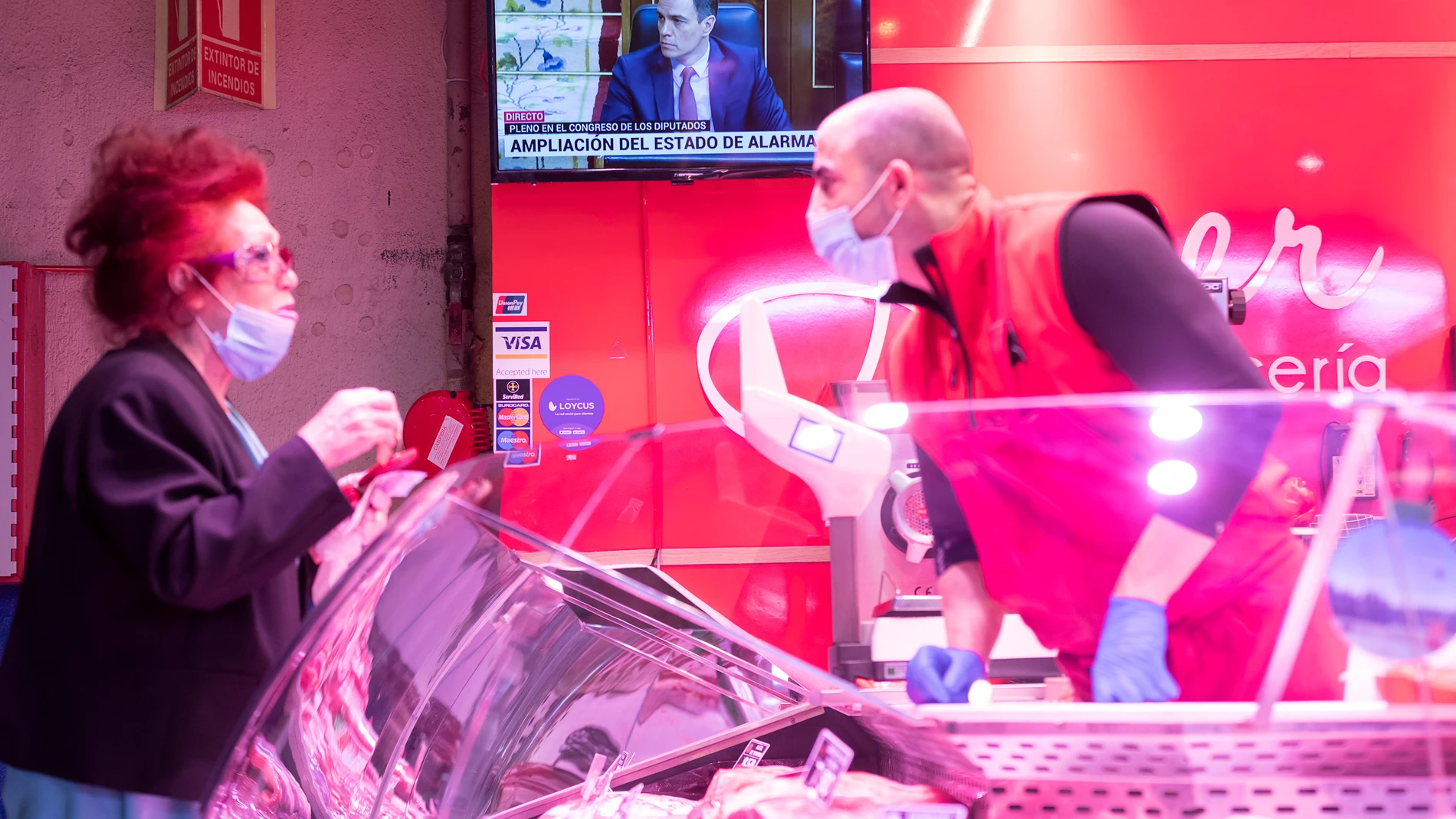 Una mujer y el empleado de un puesto del madrileño mercado de Maravillas, con Pedro Sánchez de fondo en televisión