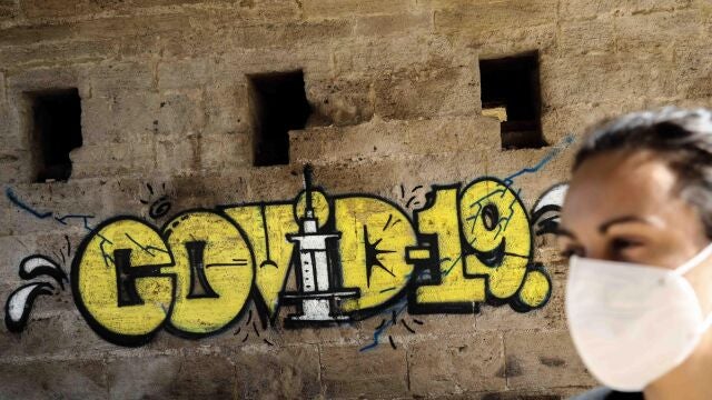 Una persona con mascarilla pasa ante un grafiti en Valencia