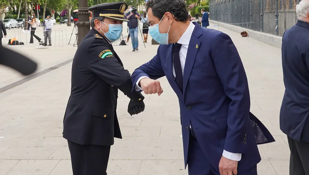 El presidente de la Junta, Juanma Moreno (d) saluda a un policía después de guardar un minuto de silencio en homenaje a las víctimas de la pandemia