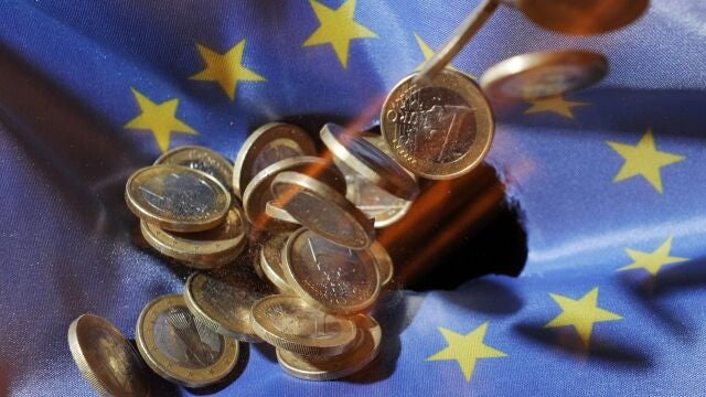Las monedas de un euro caen sobre una bandera de la Unión Europea