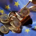 Las monedas de un euro caen sobre una bandera de la Unión Europea