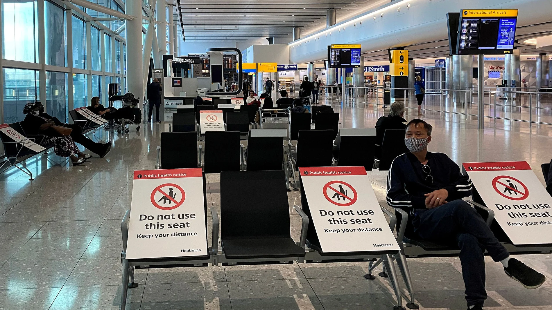 People sit amongst socially-distanced seating signs at Heathrow Airport in London
