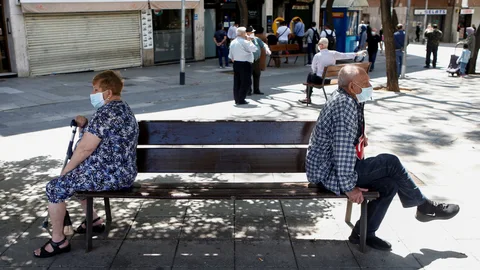 Dos ciudadanos sentados en un banco manteniendo la distancia de seguridad, en la calle Mossen Jacint Verdaguer de Santa Coloma de Gramanet (Barcelona), en plena área metropolitana.