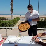 Un camarero sirve una paella en una terraza de un restaurante de la playa de la Malvarrosa de Valencia