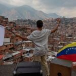 Un venezolano ondea una bandera blanca junto a otra de Venezuela en uno de los barrios pobres de Caracas
