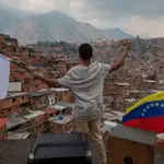 Un venezolano ondea una bandera blanca junto a otra de Venezuela en uno de los barrios pobres de Caracas