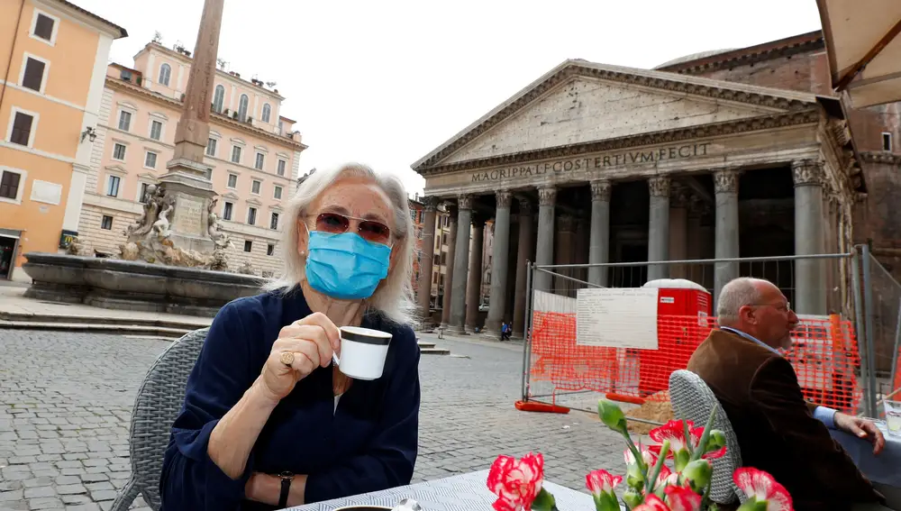 Una mujer con mascarilla con su taza de café en la plaza con el Pantéon de fondo