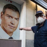 Un hombre protegido con mascarilla señala una imagen de Pedro Sánchez