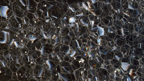 Según algunas teorías de gravedad cuántica el espacio-tiempo tendría, a escala microscópica, un aspecto similar a una espuma, como la que vemos en esta imagen. Estaría formado por “píxeles” del tamaño de la longitud de Planck, pero esos píxeles tendrían una estructura desordenada que afectaría al movimiento de los objetos. Podemos imaginar esos efectos pensando en que un objeto, para llegar de un punto A a un punto B, tendría que ir “saltando” de burbuja en burbuja, pasando cada vez a una de las burbujas adyacentes.